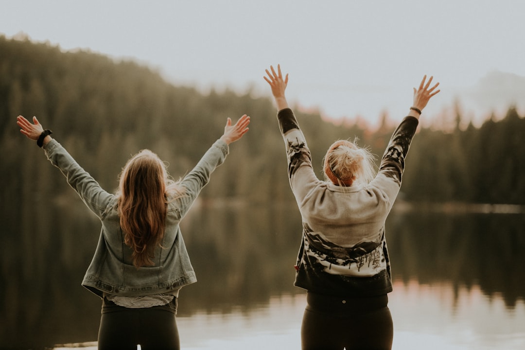 Two women with arms raised by a lake