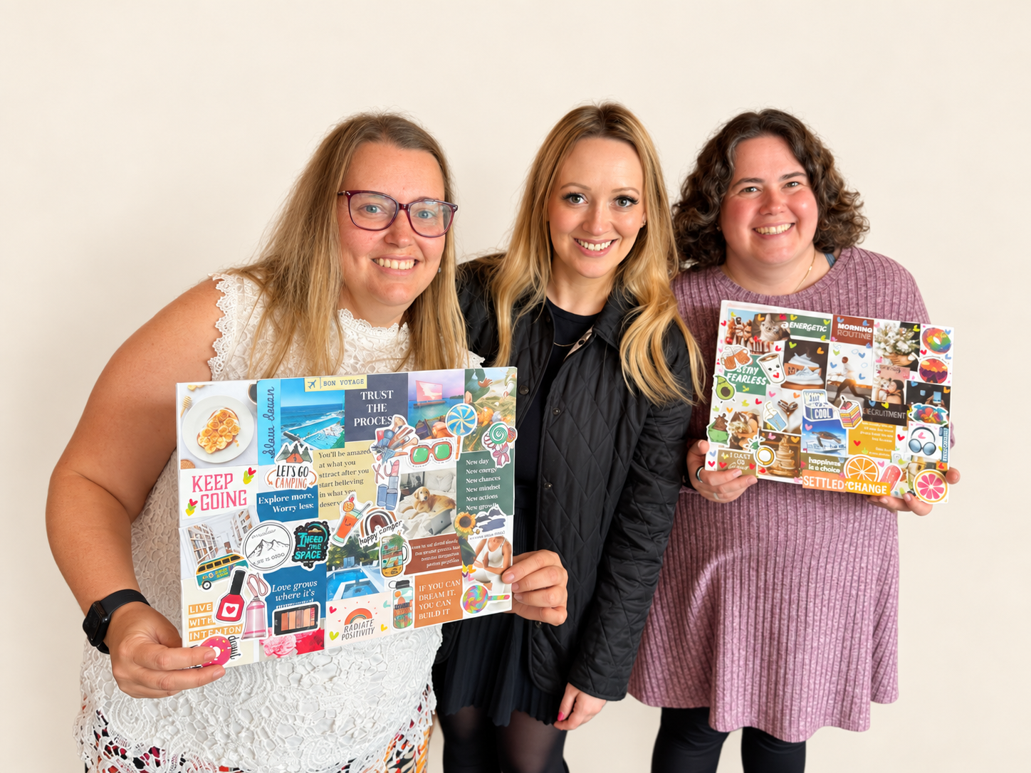 Three women smiling and holding up colorful collage vision boards at a Constellations meetup